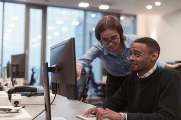 Young smiling woman explaining to serious African American coworker project strategy. Diverse startup coworkers students woman and man talking discussing working in modern office using computer.
