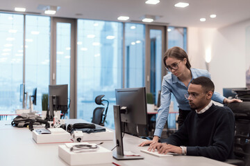 Young smiling woman explaining to serious African American coworker project strategy. Diverse startup coworkers students woman and man talking discussing working in modern office using computer.
