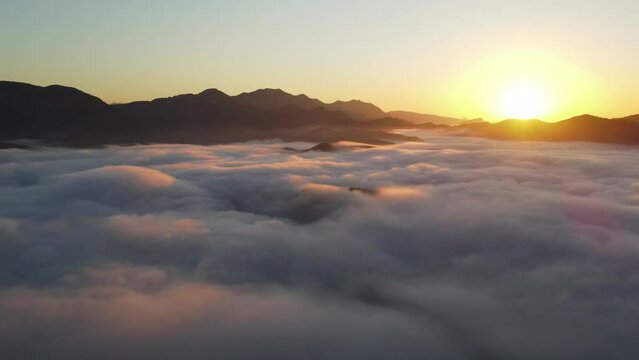 Aerial flyover of golden sunrise above the clouds in the valley of the mountains - French Alps