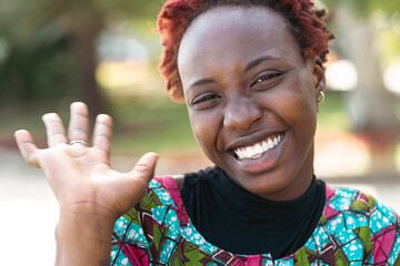 Beautiful African teenager with a big smile and a radiant expression on her face, waving at the camera; lightheartedness and ease of young people