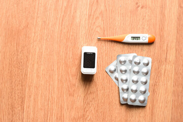 Pulse oximeter, favipiravir tablet and digital thermometer on wooden background