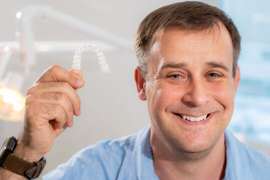Smiling orthodontist doctor holds transparent aligners in his hands