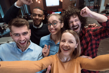 Group of business people during break from the work taking selfie picture while enjoying free time in relaxation area at modern open plan startup office. Selective focus 