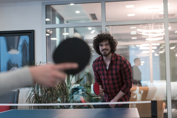 Two young start up business man playing ping pong tennis at modern creative office space people group have meeting and brainstorming in background