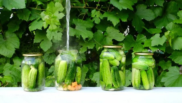 Cooking canned food from fresh cucumbers at home. Food preservation. Four cans of vegetables are on the table in garden. The main ingredients for pickling