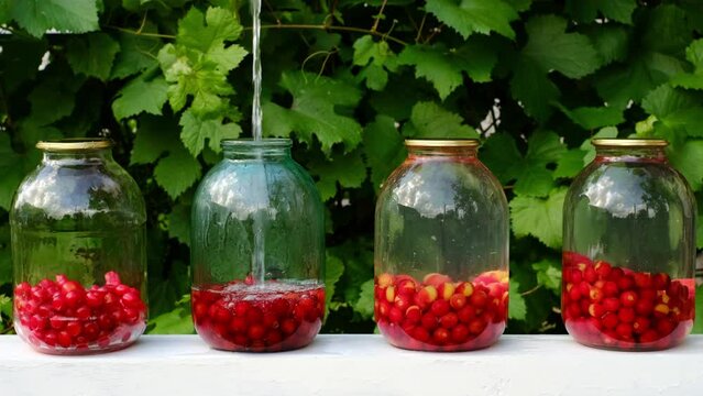 The process of homemade preparation of cherry compotes. Housewife pours boiling water into a jar with cherry fruits. Canned sweet fruit lemonades