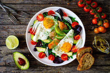Salmon salad - smoked salmon, sunny side eggs,  avocado and fresh vegetables on wooden table
