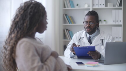 Attentive obstetrician writing down symptoms during prenatal check-up with patient