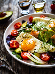 Salmon salad - smoked salmon, sunny side eggs,  avocado and fresh vegetables on wooden table
