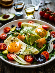 Salmon salad - smoked salmon, sunny side eggs,  avocado and fresh vegetables on wooden table
