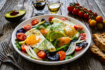 Salmon salad - smoked salmon, sunny side eggs,  avocado and fresh vegetables on wooden table
