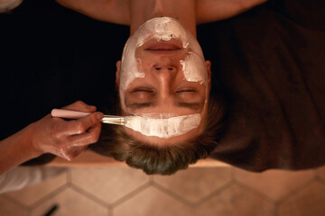 Cosmetician applying cosmetic cream on face of man