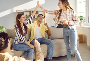 Happy excited young women give high fiving each other while having fun at home with friends. Positive cheerful women together with their boyfriends have fun together at casual gathering at home.