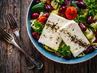 Fototapeta na wymiar Fresh Greek salad - feta cheese, cherry tomatoes, cucumber and onion on wooden table 