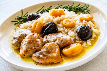 Chicken nuggets with rice, plums and apricots on white table
