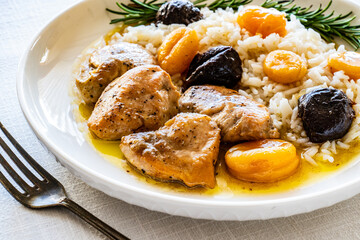 Chicken nuggets with rice, plums and apricots on white table
