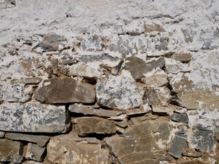 Close up of old barn facade. Stone wall with crumbling white plaster.