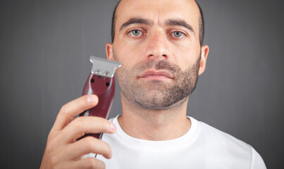 Caucasian man shaving with electric trimmer. - obrazy, fototapety, plakaty