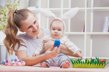 Happy Mother and baby with bunny ears playing Easter egg.