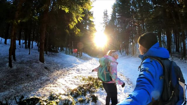 A couple on a magical hiking trail in winter in Carinthia, Austria, Europe. Morning vibes in the forest with sun beams touching the the path. Dreamy woodlands, leisure activity. Selfie stick filming

