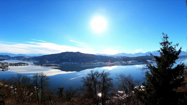 Panoramic view on the calm surface of the Woerthersee Lake in Carinthia, Austria. Lake is surrounded by high mountains. Small villages at the shores. View on Karawanks, Pyramidenkogel, Mittagskogel
