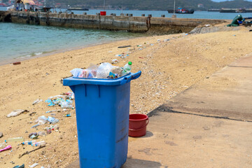 Naklejka premium Trash bin beside the sandy beach and full of plastic waste