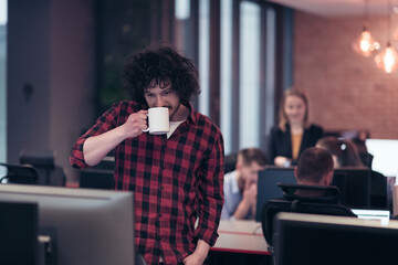 Smiling businessman in afro shirt standing in modern office with cup of coffee in hand. Selective focus 
