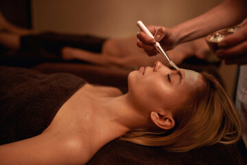 Cosmetician apply clay mask on face of relax woman