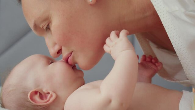 Mother playing and kissing her a newborn baby.  Happy mom spends time with her baby. Face of cute baby looking at mom. Mama is kissing her infant boy. Motherhood and family. Slow motion footage.