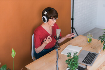 Mature woman making podcast recording for her online show. Attractive business woman using...