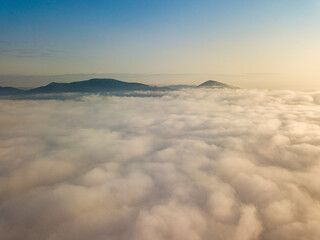 Flight over fog in Ukrainian Carpathians in summer. Mountains on the horizon. Aerial drone view.