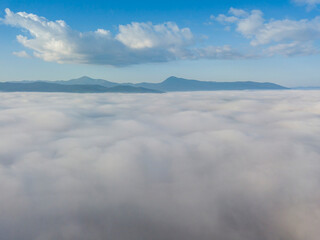 Flight over fog in Ukrainian Carpathians in summer. Mountains on the horizon. A thick layer of fog covers the mountains with a continuous carpet. Aerial drone view.