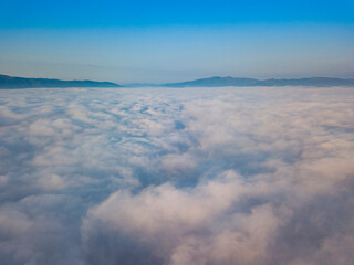 Flight over fog in Ukrainian Carpathians in summer. Mountains on the horizon. Aerial drone view.