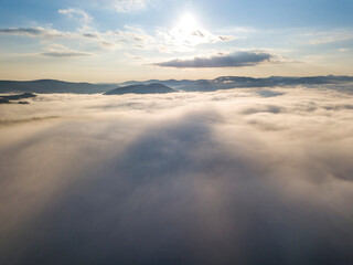 Flight over fog in Ukrainian Carpathians in summer. Mountains on the horizon. A thick layer of fog covers the mountains with a continuous carpet. Aerial drone view.