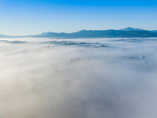 Flight over fog in Ukrainian Carpathians in summer. Mountains on the horizon. A thick layer of fog covers the mountains with a continuous carpet. Aerial drone view.