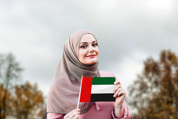 Muslim woman in hijab holds flag of United Arab Emirates
