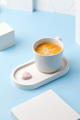 One white coffee cup with espresso or cappuccino on beton tray and podiums. Aroma. Mug of coffee. Blue background. Modern