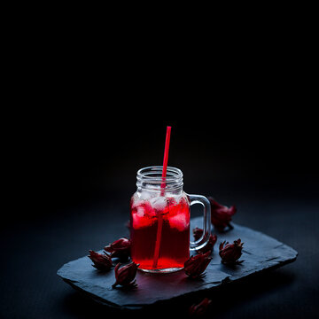 Fresh Roselle fruit, Jamaica sorrel, Rozelle or hibiscus sabdariffa) on black stone and glass of roselle juice.