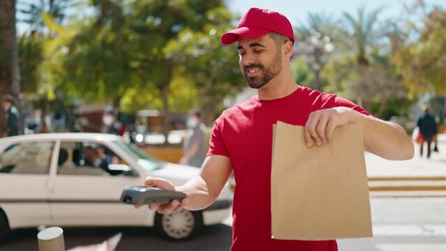 Young hispanic man deliveryman holding deliver paper bag at park