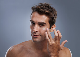 Even men like to be soft..... Studio shot of a handsome young man applying cream to his face.