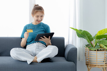 A woman playing smartphone on the sofa in her home living room, she is relaxing on weekends after a hard day's work, she is shopping online and paying by credit card. Credit card payment concept.