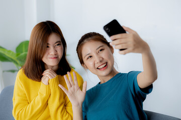 Two women in the living room, they are waving to their friends in a smartphone video calling program, they are spending their vacations watching movies and listening to music together.