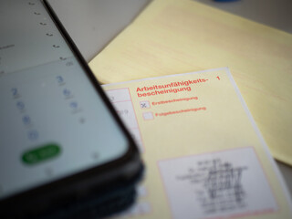 German sick certificate and smartphone with number pad: sick leave by telephone, digital sick note