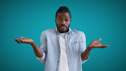 Young black male showing no idea gesture on blue background, feeling confused, doubt