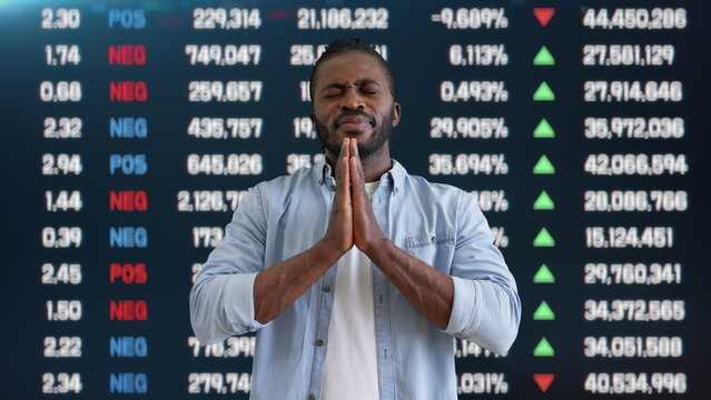 Praying young man joining hands with stock market data on background, luck