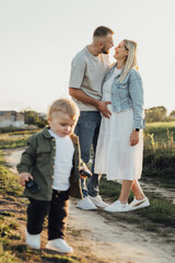 Fototapeta premium Happy Young Family Outdoors, Father Holding His Pregnant Wife by Belly While Their Toddler Son Playing Around Them