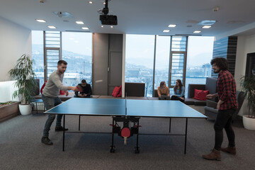 Two young start up business man playing ping pong tennis at modern creative office space people...
