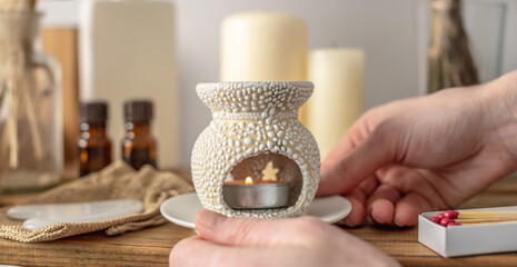 There is an aroma lamp in women's hands, candles and oils on the table. Concept of aromatherapy,...