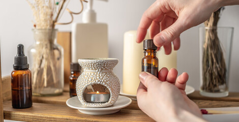 Hand is holding a bottle of essential oil and opening the lid. There is an aroma lamp, candles and...