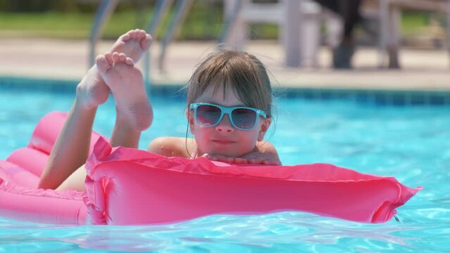 Young child girl relaxing on summer sun swimming on inflatable air mattress in swimming pool during tropical vacations. Summertime activities concept